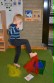In der Bildmitte steht ein Junge, er steht auf einem Bein und hält mit dem anderen Fuß ein rotes Tuch in der Luft, er probiert das Tuch in eine Kiste zu legen
