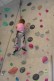 Ein Mädchen klettert an der Kletterwand. Das Sicherungsseil ist schräg durchs Bild zu sehen. Das Mädchen hat noch ein kleines Stück vor sich, bis es den höchsten Punkt erreicht hat.