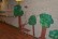 An die Wände des Kindergartenflures sind große aus Tonpappe gebastelte Bäume geklebt. Davor steht ein Hirsch, ebenfalls aus Tonpappe und Geweih aus Zweigen. Weiter im Hintergrund sieht man an der Wand des Flures gebastelte Frischlinge und ein Wildschwein. Darüber hängen verschiedene Fotos. 
