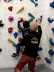 Ein Junge klettert ohne Seil an einer niedrigen Kletterwand. Hinter ihm kniet ein Trainer der „Bergstation“ und zeigt auf den nächsten Griff.