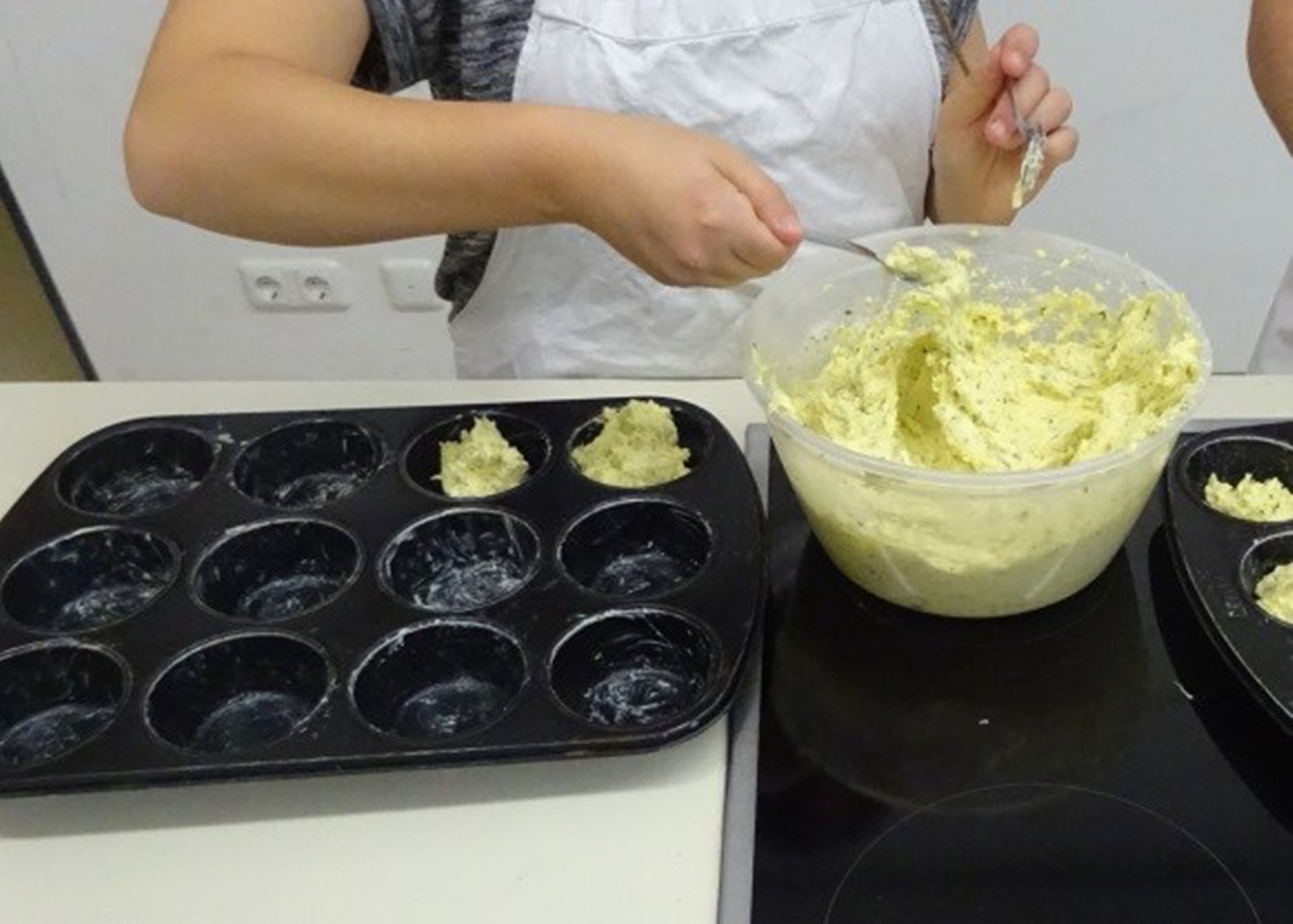 Hände portionieren Teig mit Löffeln in eine Backform für Muffins.