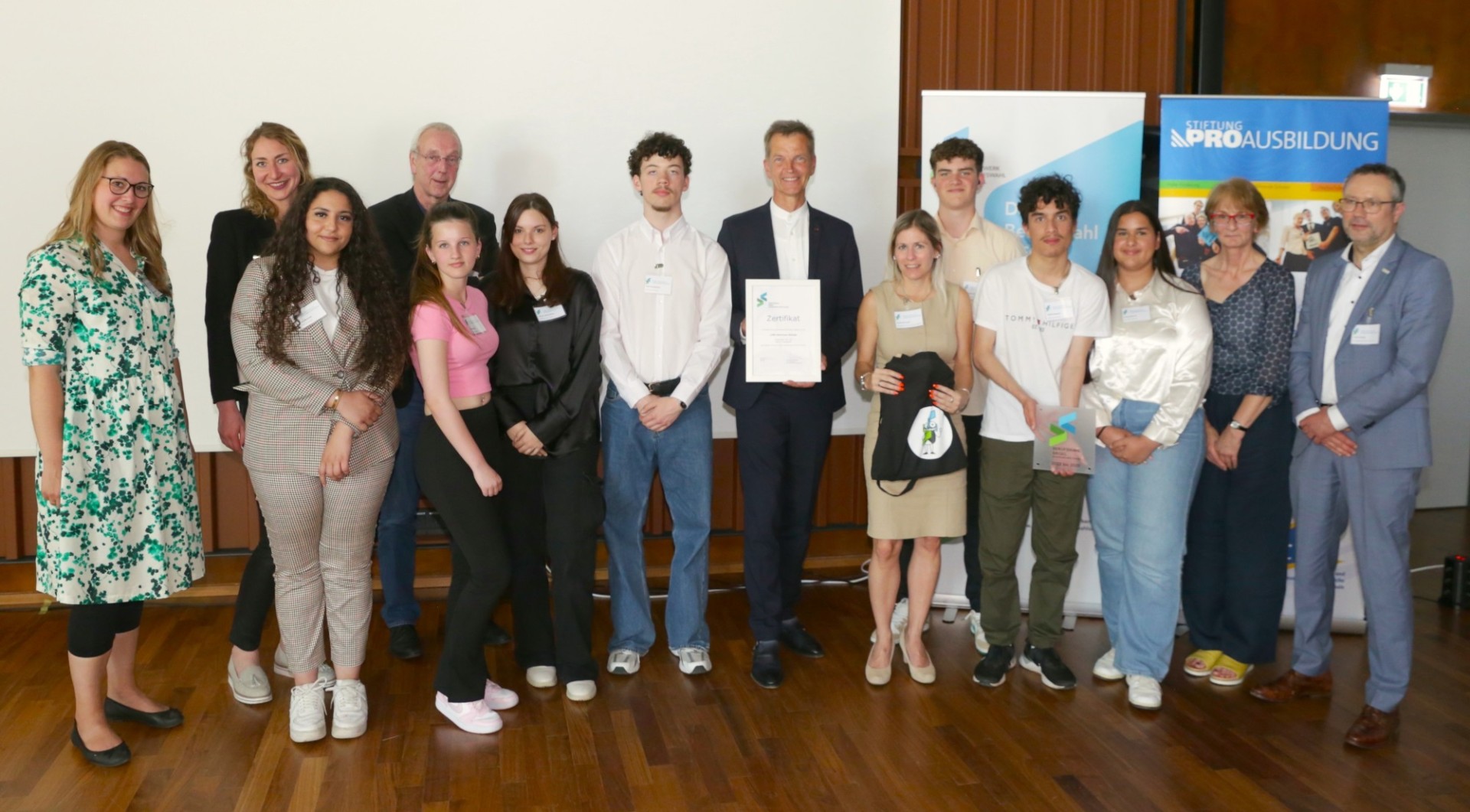 Eine Gruppe von Schüler*innen und Lehrkräften präsentiert stolz das verliehene Berufswahl-Siegel für ausgezeichnete Berufsorientierung.