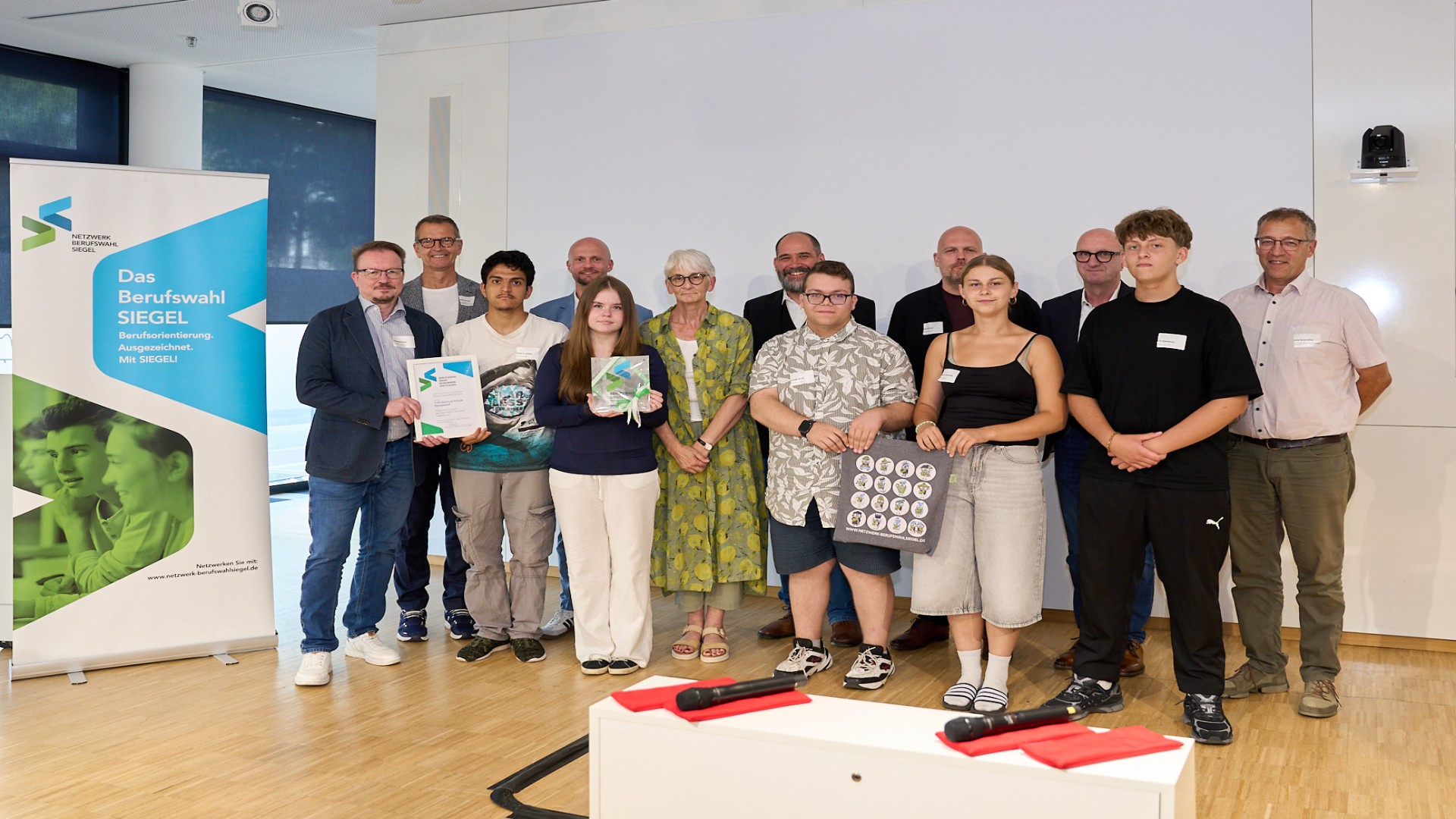 Eine Gruppe von Schüler*innen und Lehrkräften präsentiert stolz das verliehene Berufswahl-Siegel für ausgezeichnete Berufsorientierung.